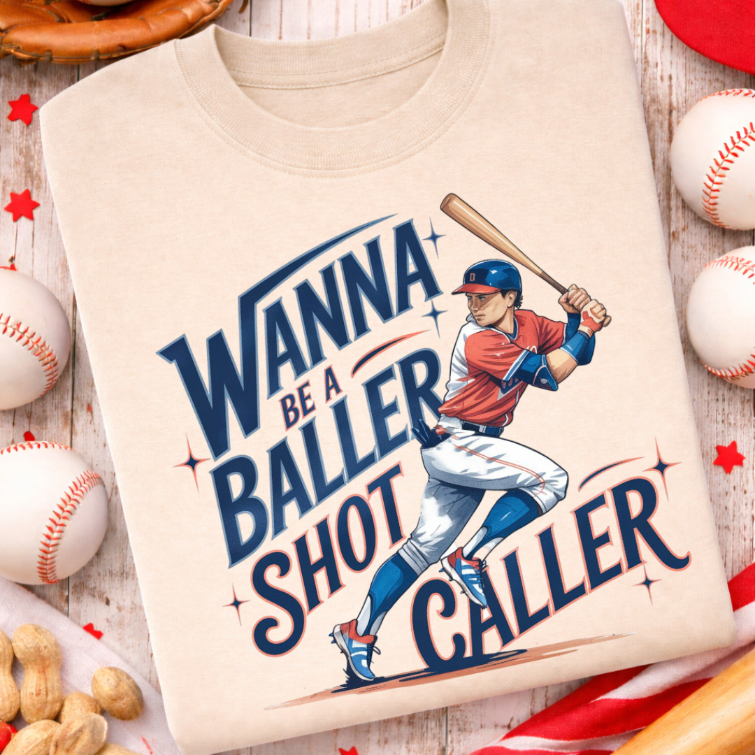 Sand graphic tee featuring the phrase "Wanna Be a Baller, Shortstop Caller" with a baseball player illustration and vintage-inspired lettering.
