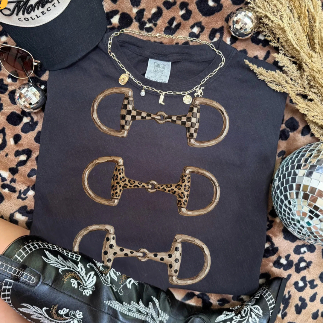 Washed black Comfort Colors graphic tee featuring three western horse bit designs with checkered, leopard, and spotted patterns.