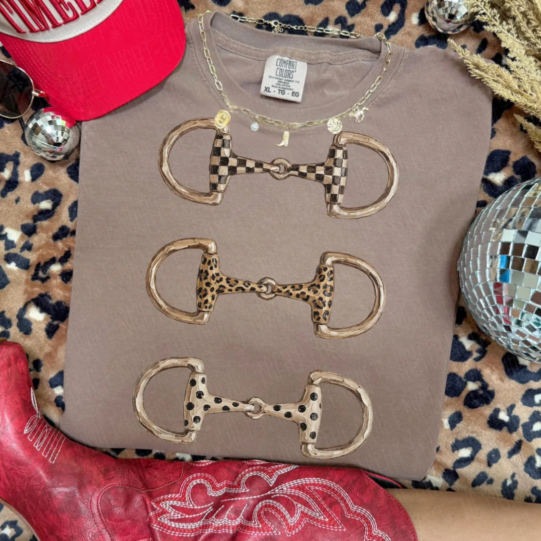 Taupe Comfort Colors graphic tee featuring three western horse bit designs with checkered, leopard, and spotted patterns.