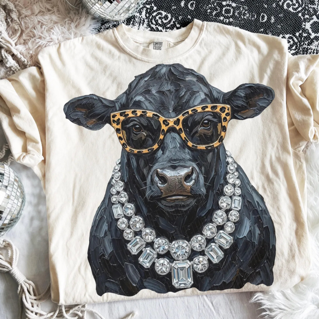 Natural graphic tee featuring a fashionable Black Angus cow wearing leopard print sunglasses and layered crystal statement necklaces in a hand-painted style.
