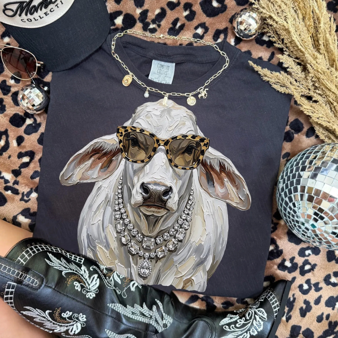 Pepper black graphic tee featuring a stylish white cow wearing leopard print sunglasses and layered crystal statement necklaces in a hand-painted western art style.