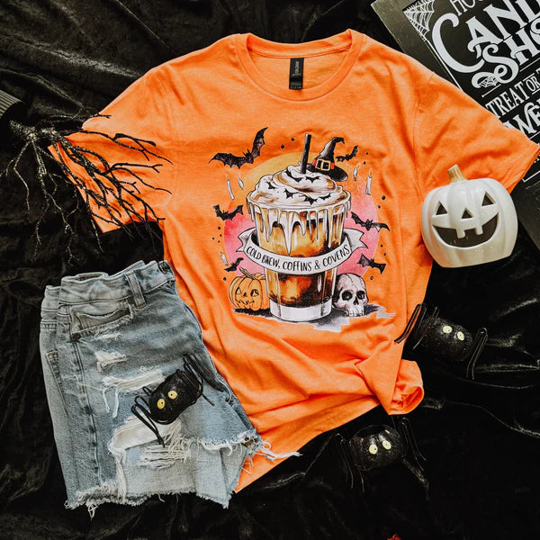 Orange t-shirt with Halloween-themed cupcake design, denim shorts, and small pumpkin on a dark background