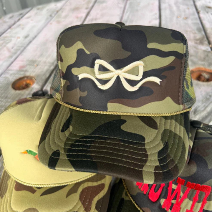 Camouflage trucker hat featuring a feminine embroidered bow design with an adjustable mesh back.