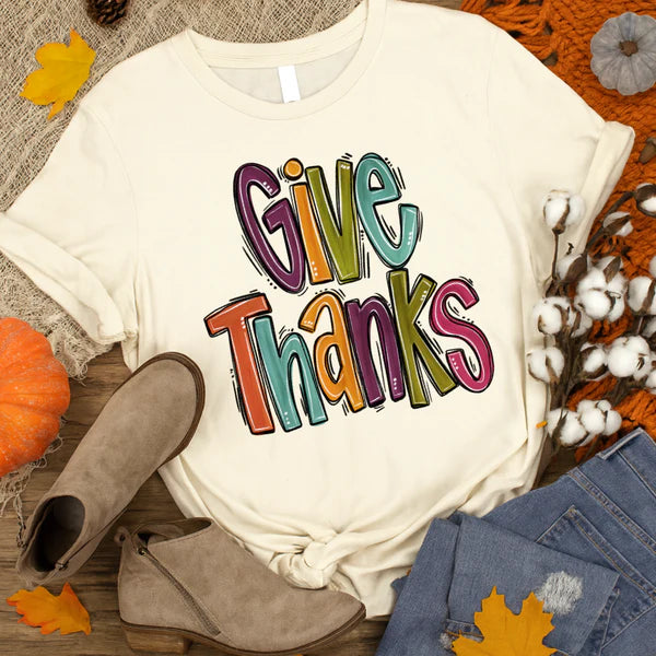 White t-shirt with 'Give Thanks' text, surrounded by autumn-themed items like pumpkins and leaves.