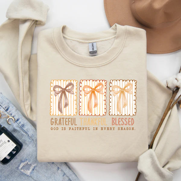 Tan sweatshirt with decorative text and ribbons on a white surface with accessories.