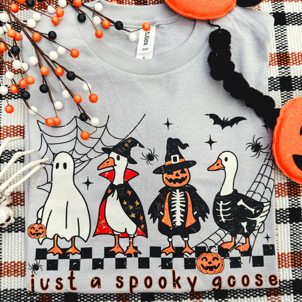Gray t-shirt with Halloween-themed design of geese in costumes on a checkered fabric background.