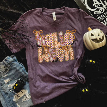 Purple t-shirt with Halloween-themed design on a dark background with pumpkins and denim shorts.