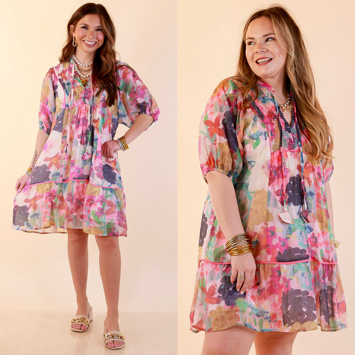 Models are wearing Floral Print Smocked Yoke Dress with Tie Neckline and Puff Sleeves in Pink Mix against a beige backdrop. 