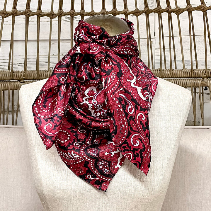 Mannequin head with a pink patterned scarf on a white cushioned chair with wicker backrest.