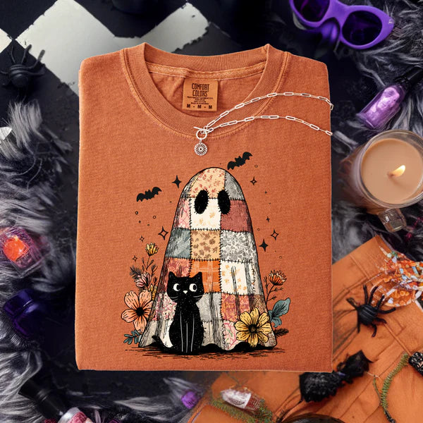 Folded orange shirt with ghost and black cat design on a Halloween-themed background