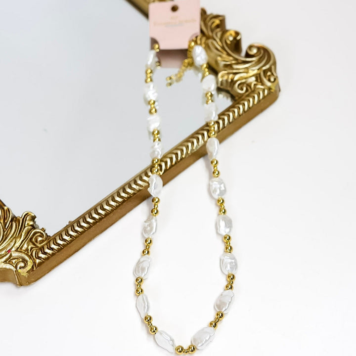 A pearl and gold necklace over a mirror on a white background.