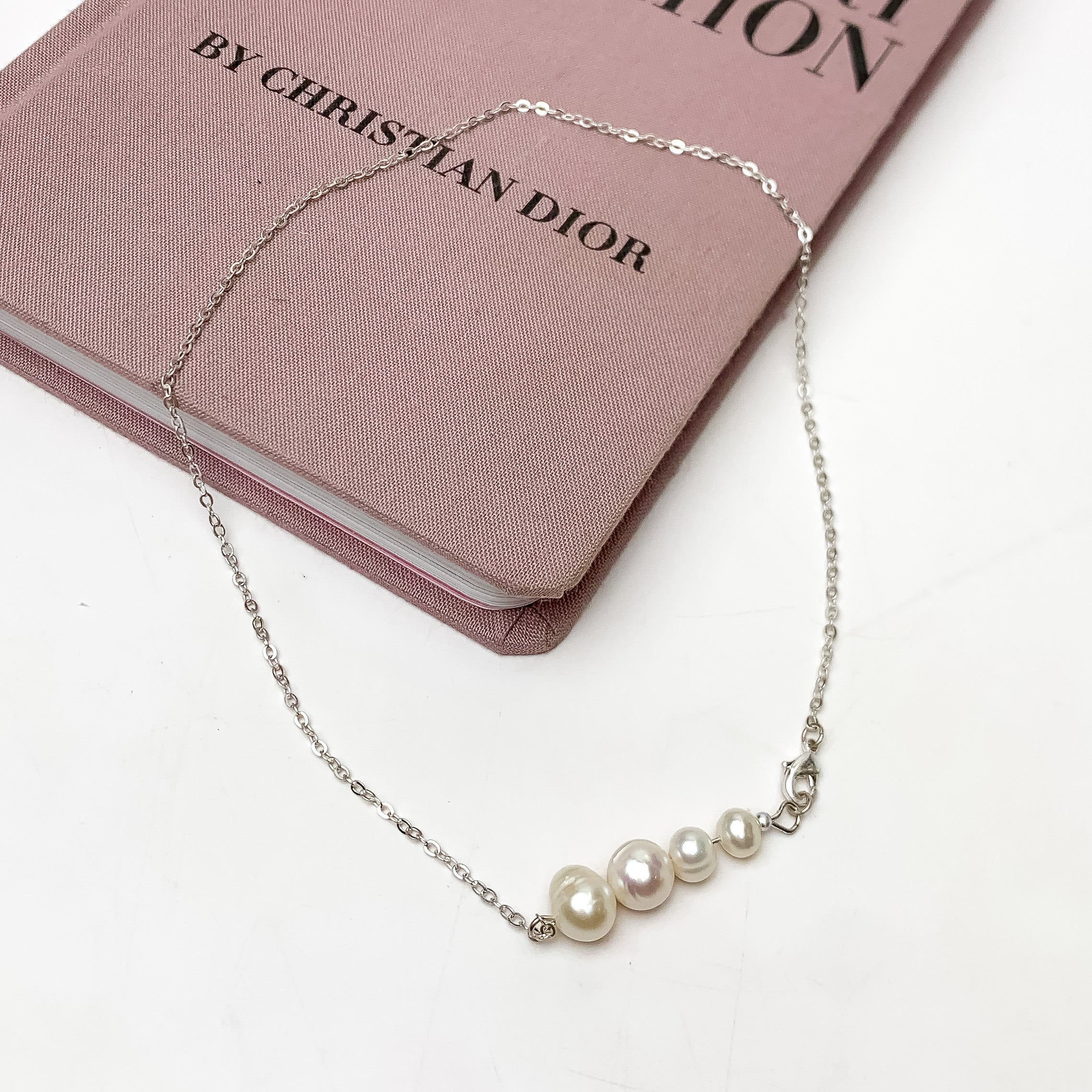 Connecting Pearls Silver Tone Necklace. This necklace is pictured on a white background with part of it on a pink book.