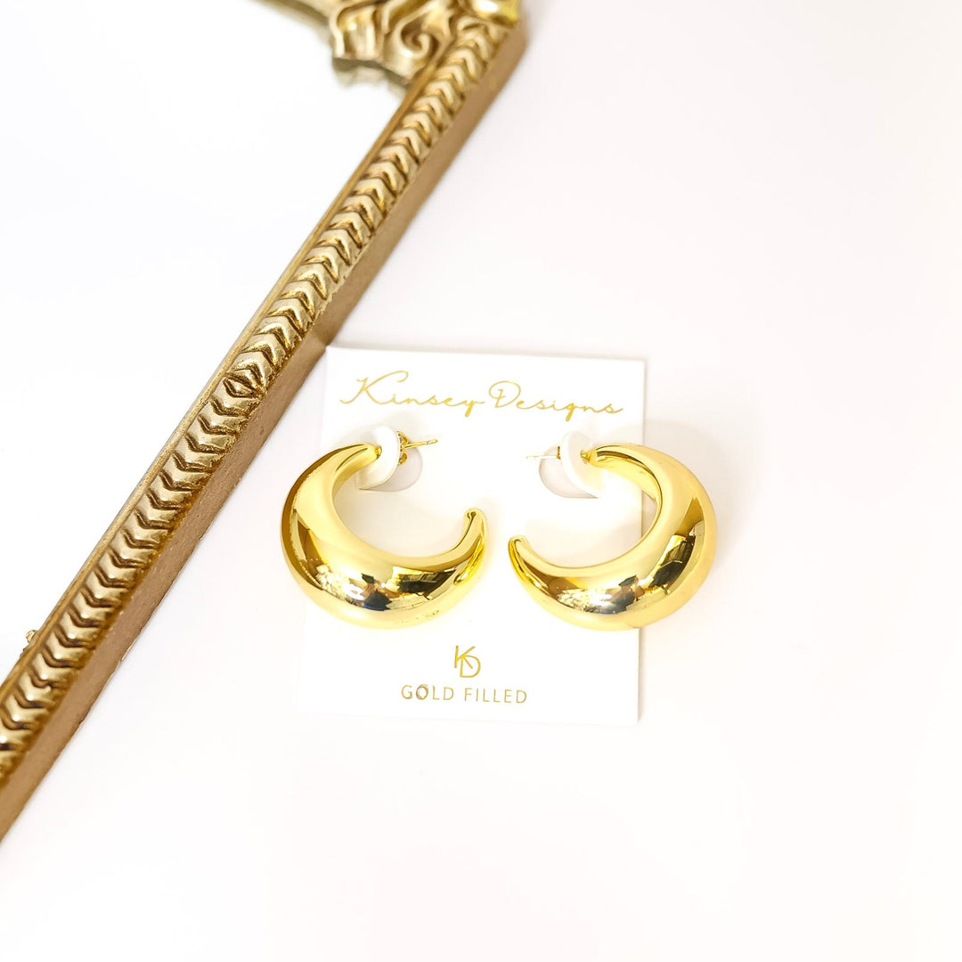 Gold hoop earrings on a white card with a gold handle in the background