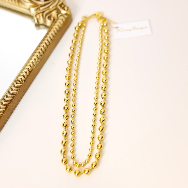 Gold chain necklace on a white surface with a decorative gold frame.