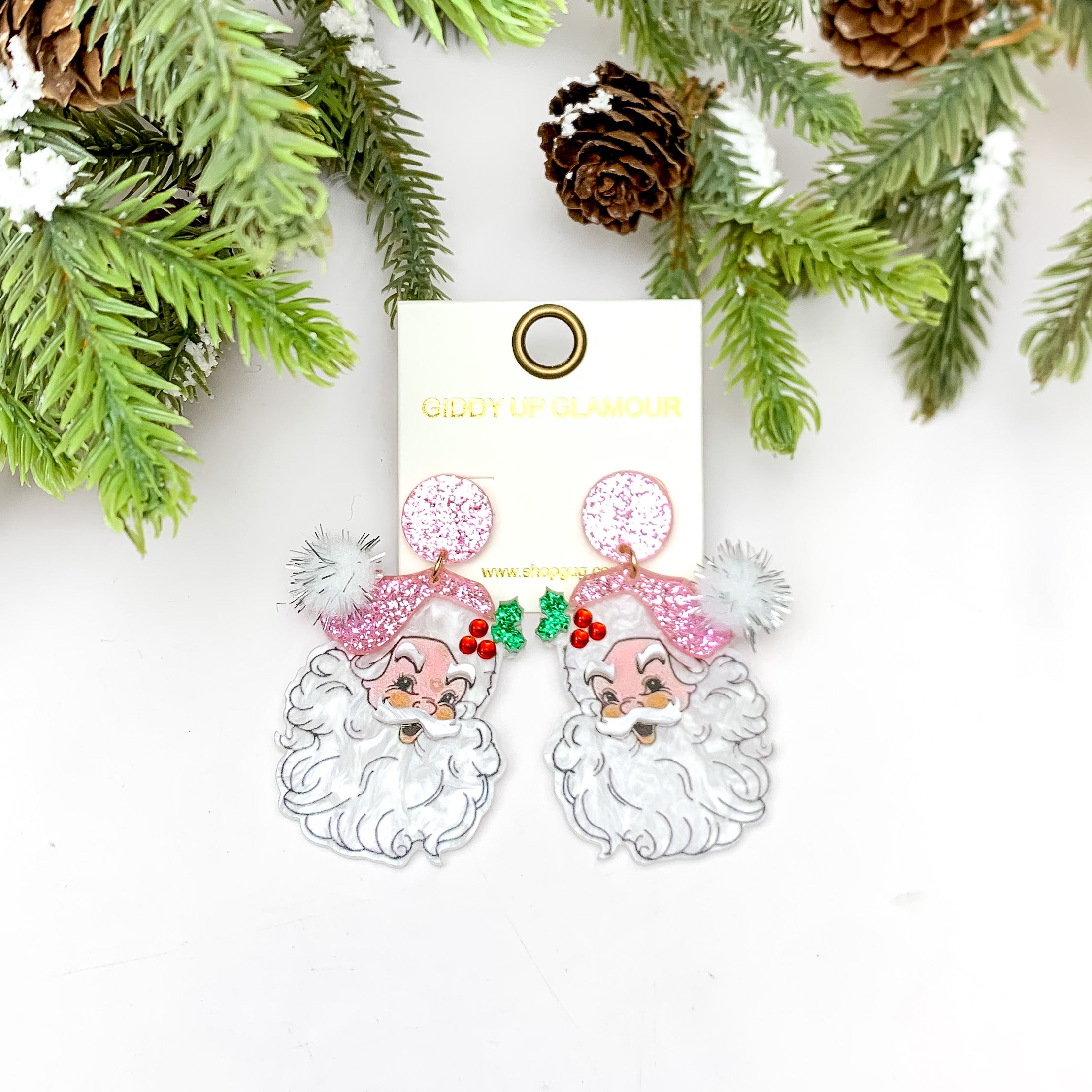 Glittery Pink Santa Earrings With Pom. These earrings are pictured on a white background with a tree and pine cones at the top.