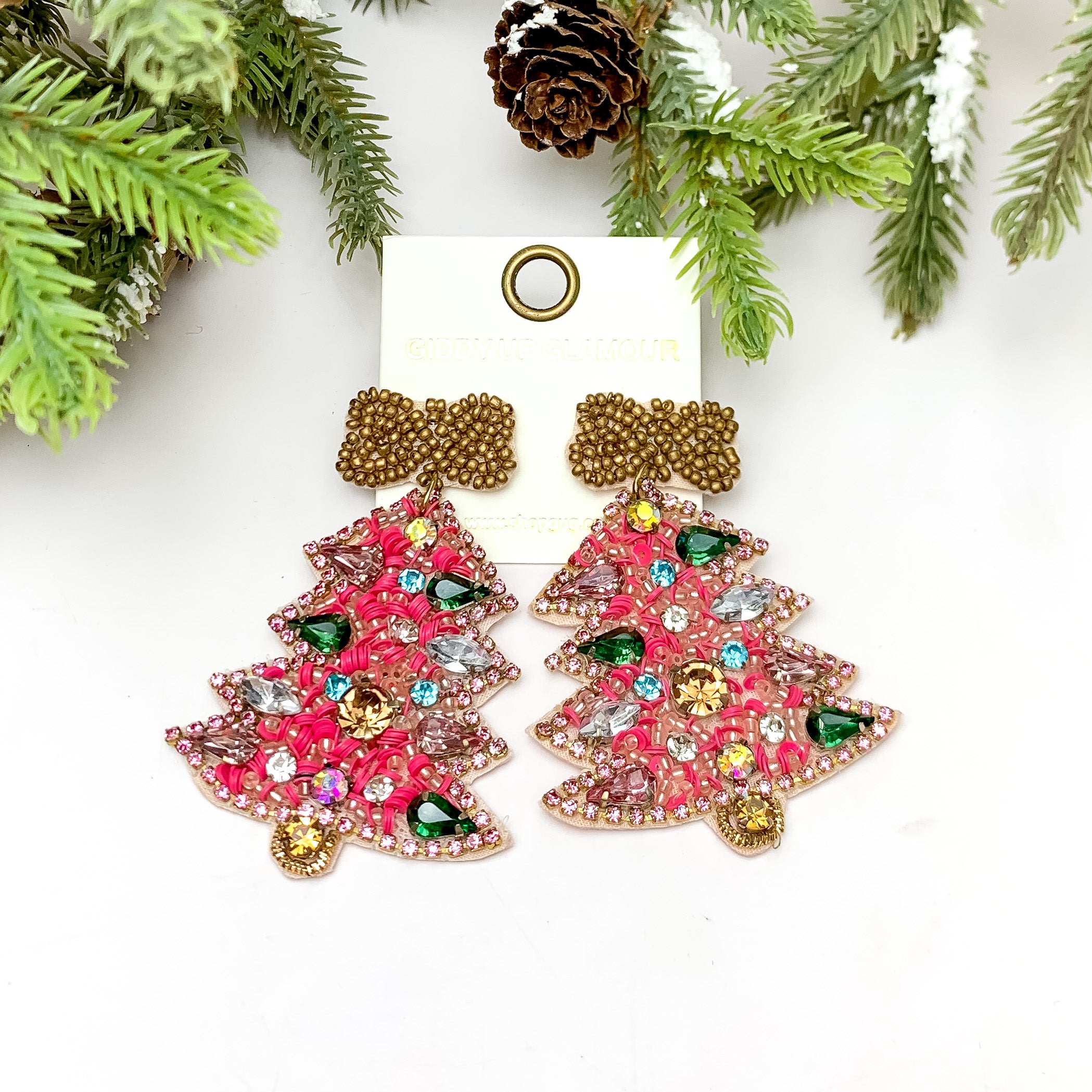 Multicolor Crystals and Pink Beaded Christmas Tree Earrings With a Gold Bow. These earrings are pictured on a white background with a tree and pine cones at the top.