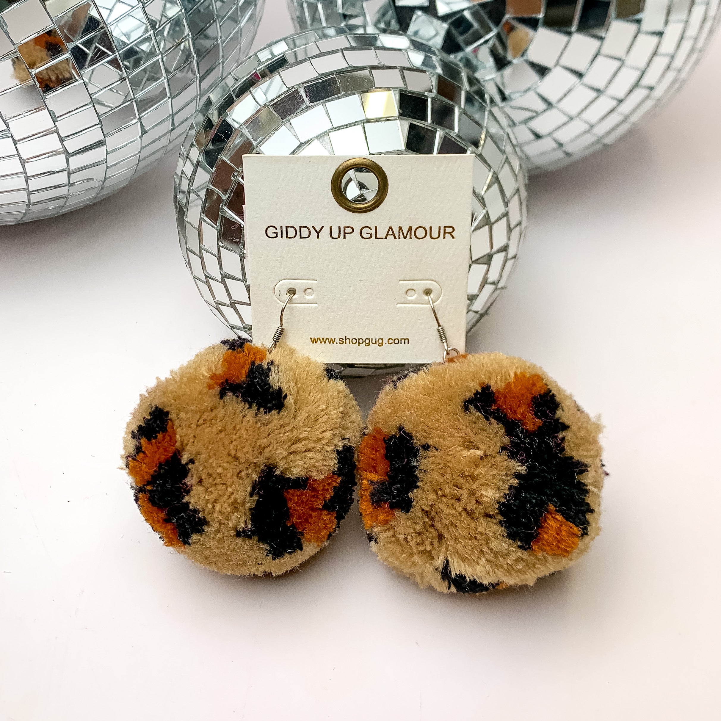 Party Poms Large Leopard Print Earrings in Brown. These earrings are on a white background with disco balls above them.