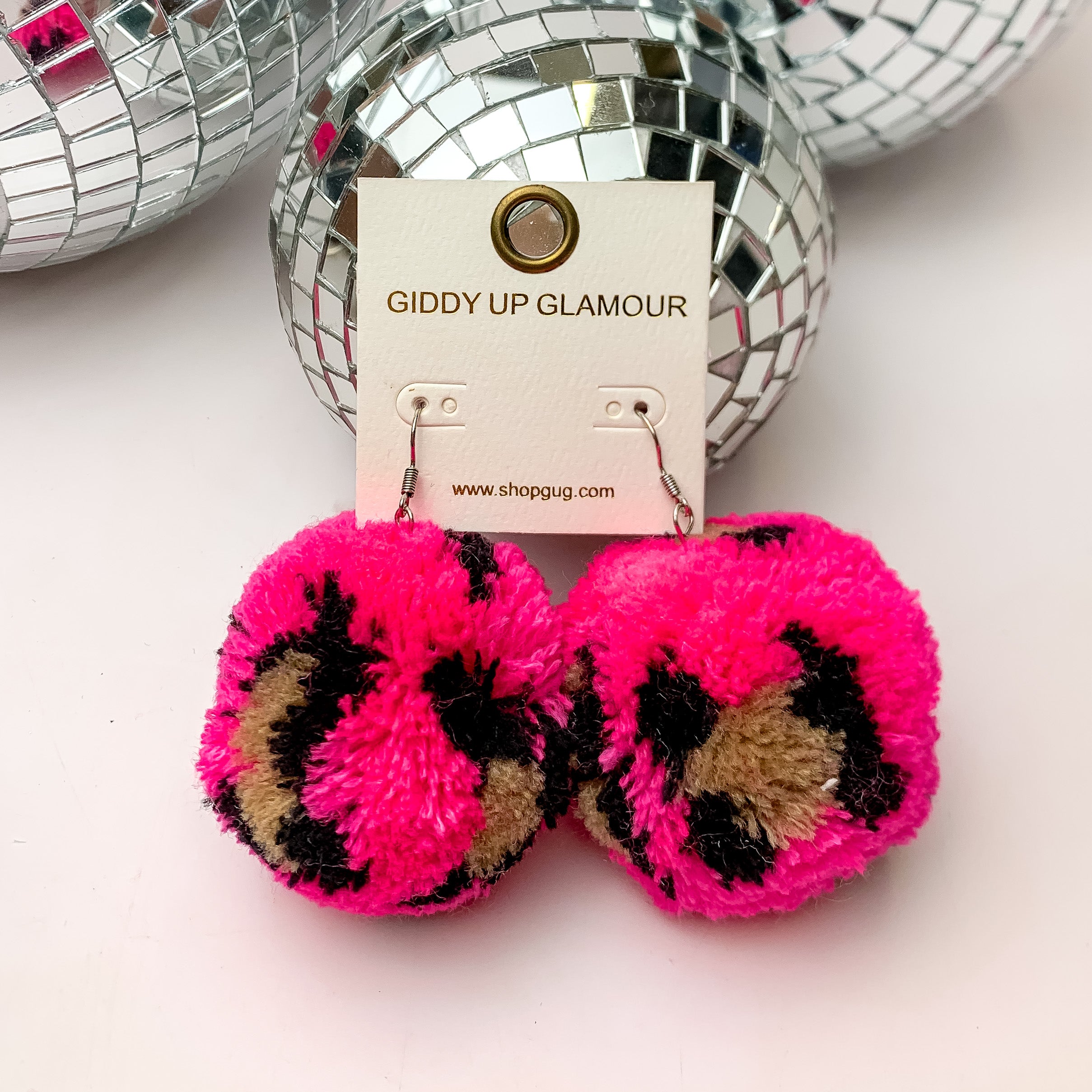 Party Poms Large Leopard Print Earrings in pink. These earrings are on a white background with disco balls above them.
