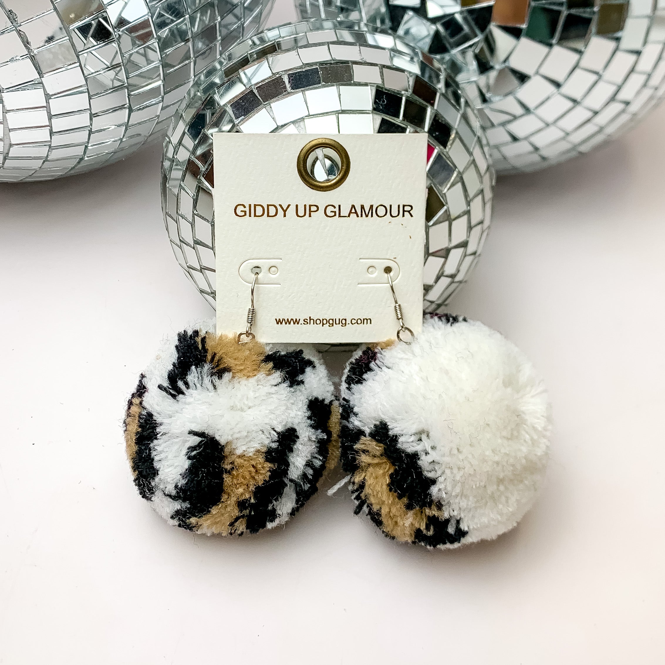 Party Poms Large Leopard Print Earrings in White. These earrings are on a white background with disco balls above them.