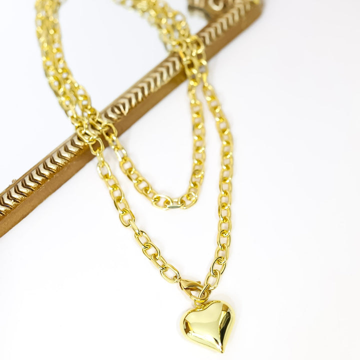 Gold chain necklace with a heart charm on a white background