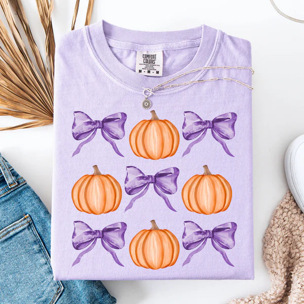 Purple t-shirt with pumpkin and bow pattern on a white surface