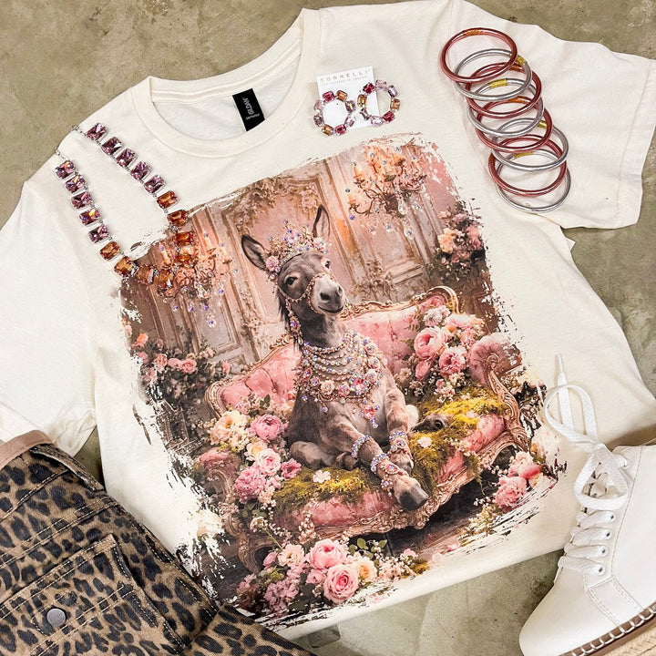 White t-shirt with a donkey and floral design, leopard print pants, and white sneakers on a concrete floor.