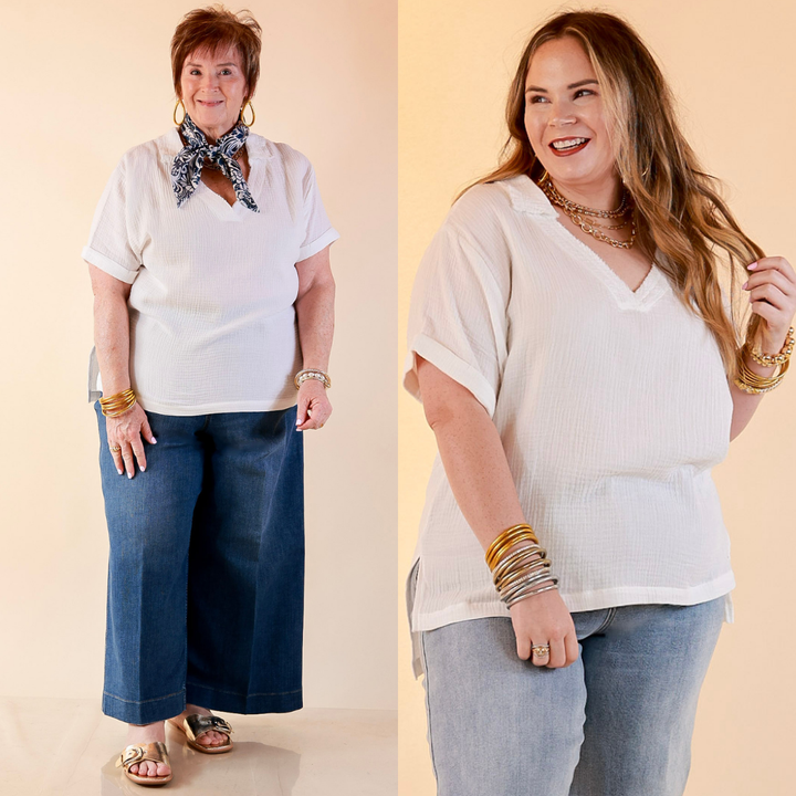 Models are wearing Short Sleeve Collared V-Neck Linen Top with Rolled Sleeve Detail in White with Jeans against a beige backdrop. 