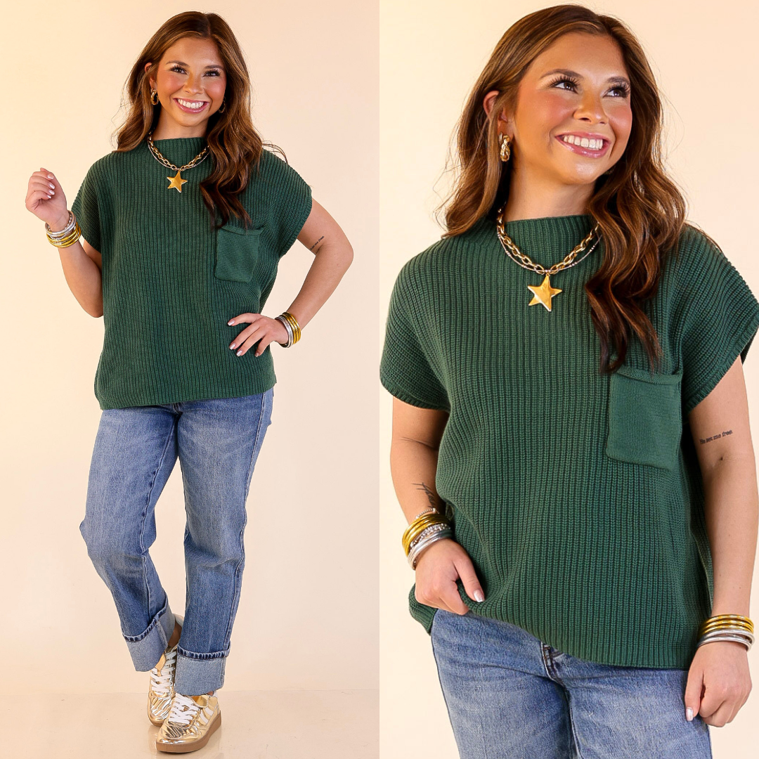 Woman wearing Cap Sleeve Sweater with Front Pocket in Forest Green and blue jeans on a beige background