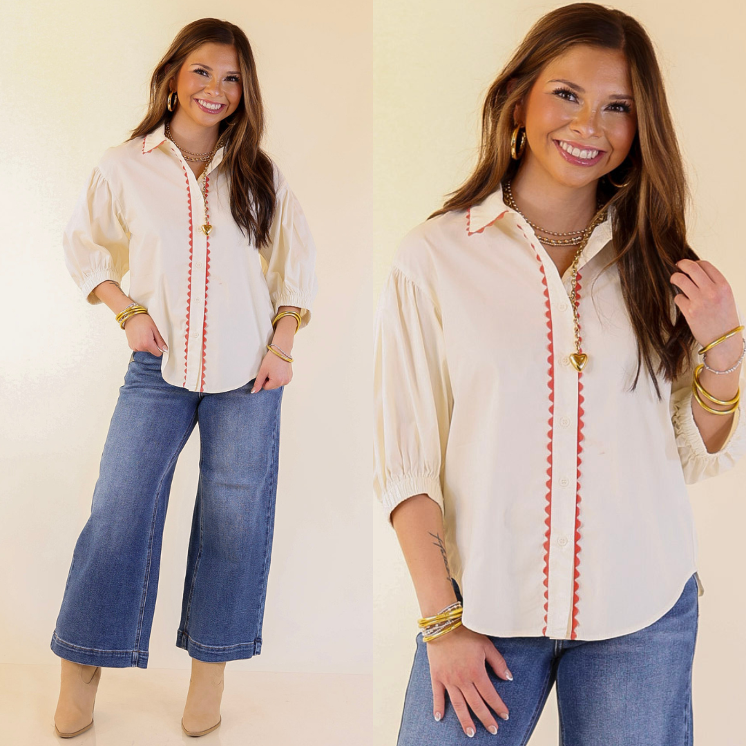 Woman wearing a cream blouse with pink stitching and blue jeans on a plain background