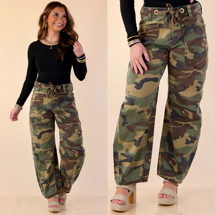 Model is wearing Risen Wide Leg Barrel Jeans in camo with a black top against a beige background. 