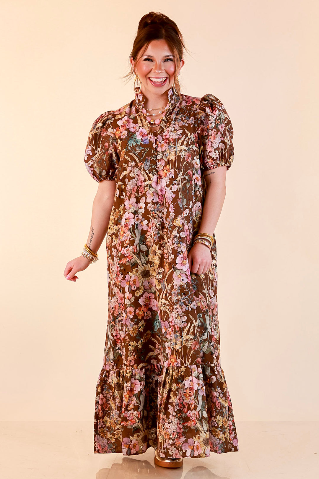 Model wearing a brown floral eyelet maxi dress with a ruffled collar, puff sleeves and ruffle hem.