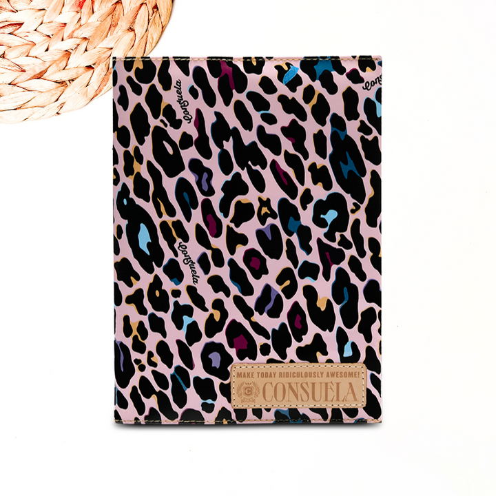 A solid white background with a wooded decor decal and a reusable notebook case made by consuela. The case is printed in a colorful jag and has a genuine leather consuela logo.