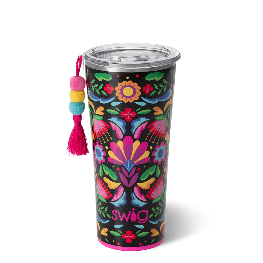 Caliente 22 oz tumbler. This Cup has a black background and features vibrant color designs on top of it. The cup also has a charm hanging from it. The background of the picture is white.