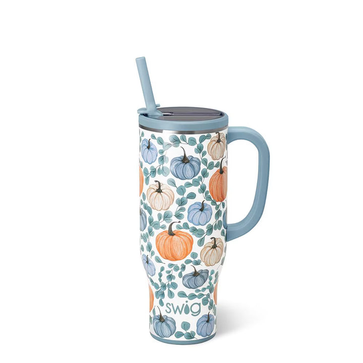 A handled travel tumbler with a lid and straw, featuring a white background decorated with a pattern of orange, blue, and beige pumpkins and green leaves. The handle, lid, straw, and base are in a dusty light blue color.