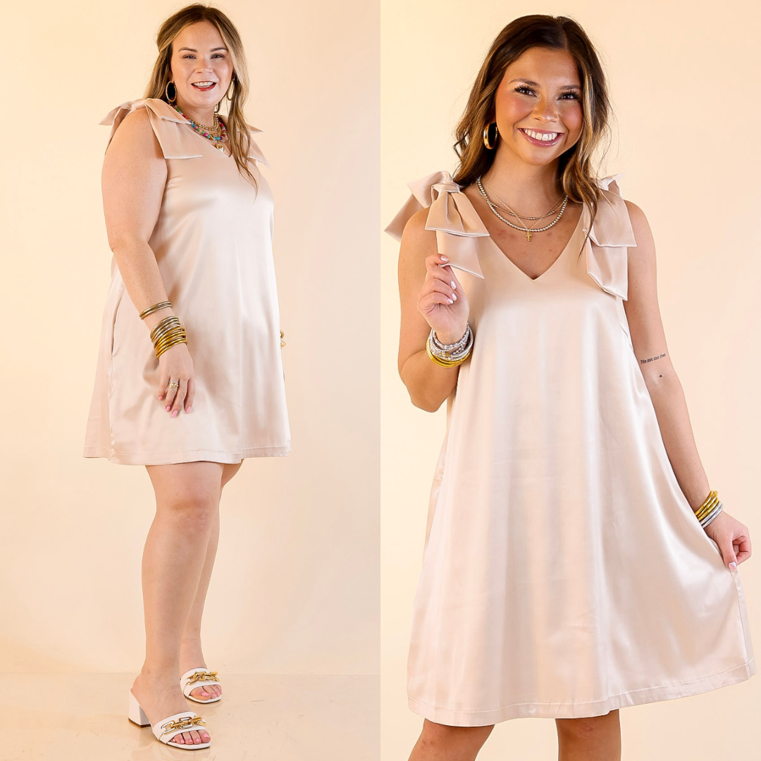 Models are wearing V-neck mini dress with bow strap detailing in champagne  on a beige background