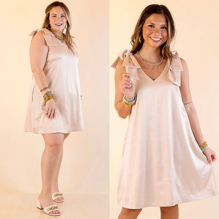 Models are wearing V-neck mini dress with bow strap detailing in champagne  on a beige background