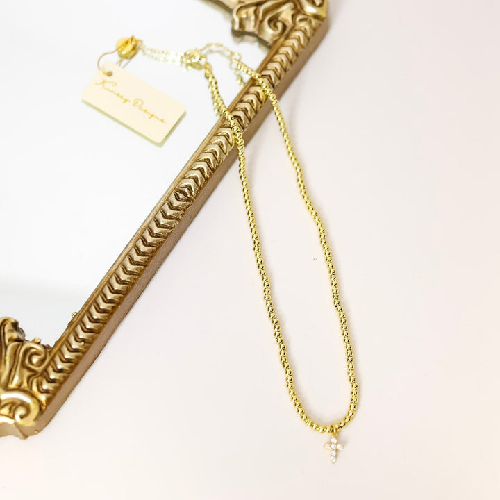 Gold necklace with a crystal cross pendant and decorative frame on a white background