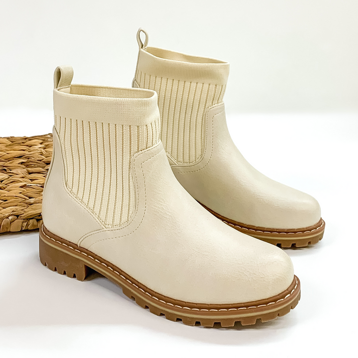 Slip on booties in cream with a tan, rubber sole. These boots are pictured on a white background. 