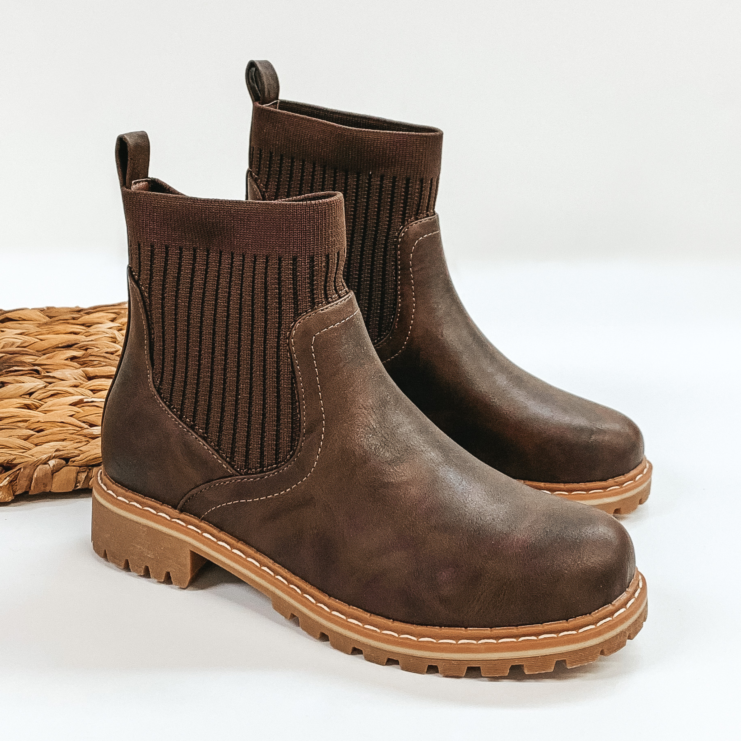 Slip on booties in brown with a tan, rubber sole. These boots are pictured on a white background. 