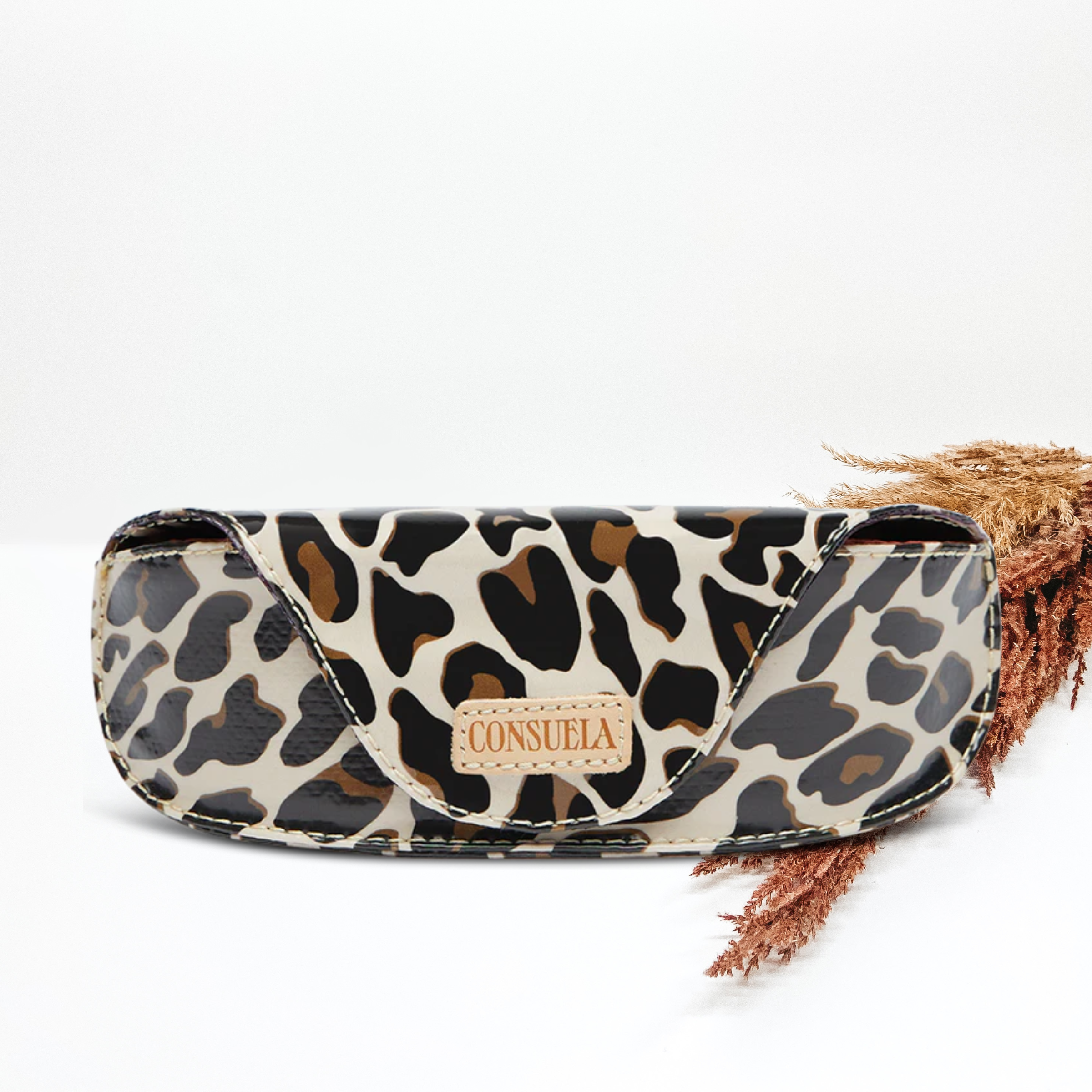 Sunglass case in a leopard print and light tan Consuela patch on the front. This tote is pictured in front of pompous grass on a white background.
