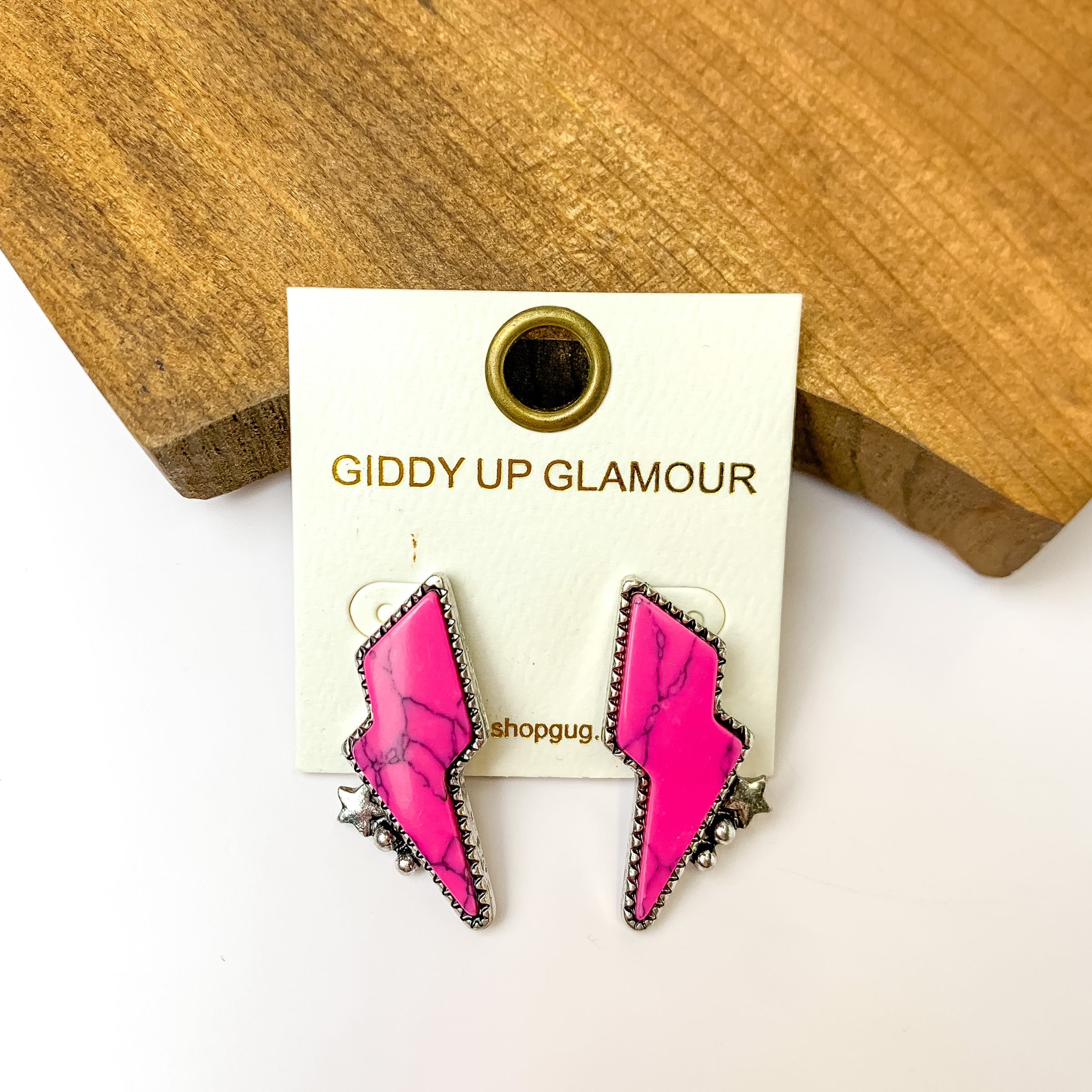 Driving Down Lightning Bolt Stone Post Earrings in Hot Pink with Silver Detailing. Pictured on a white background sitting against a piece of wood.