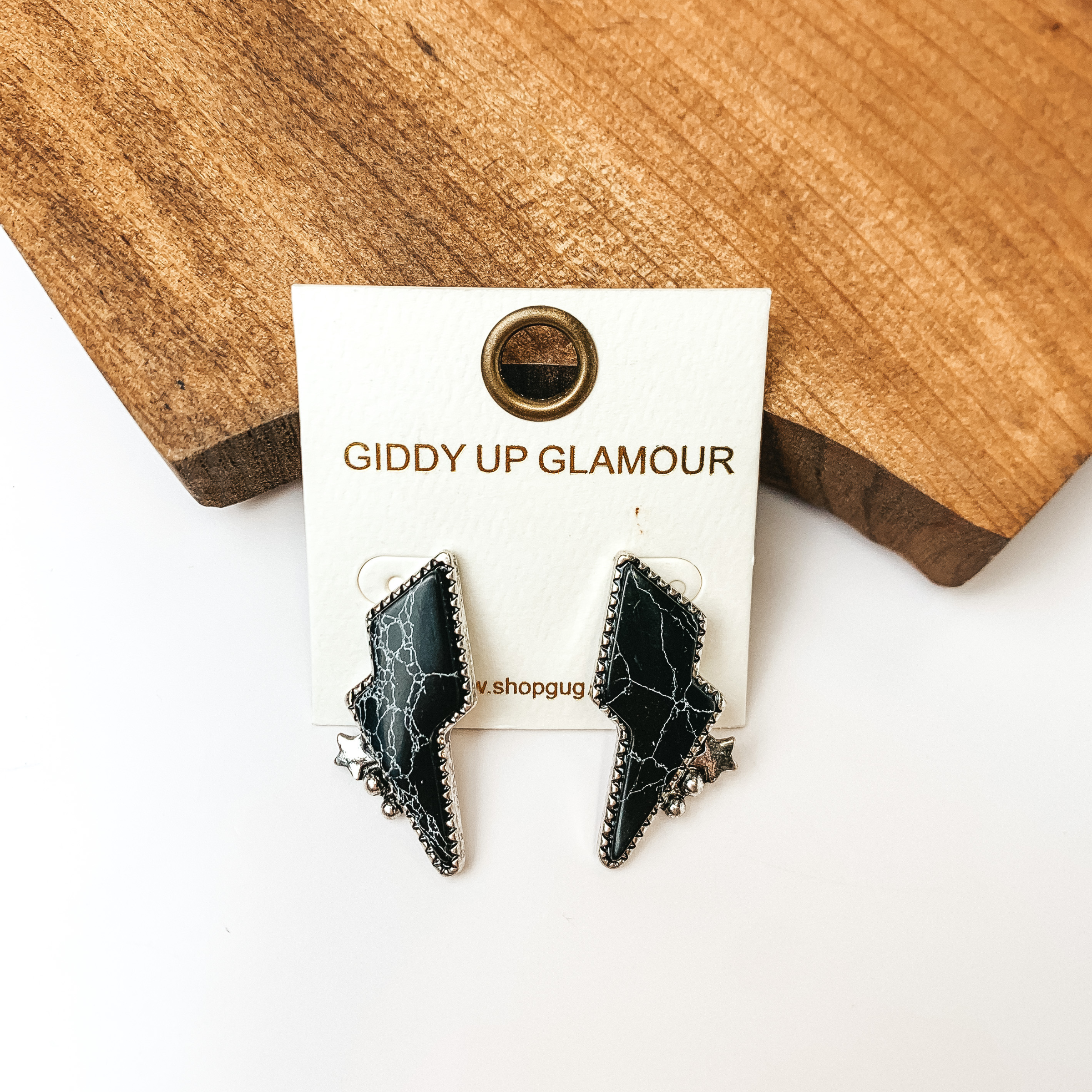 Driving Down Lightning Bolt Stone Post Earrings in Black with Silver Detailing. Pictured on a white background with the earrings against a piece of wood.
