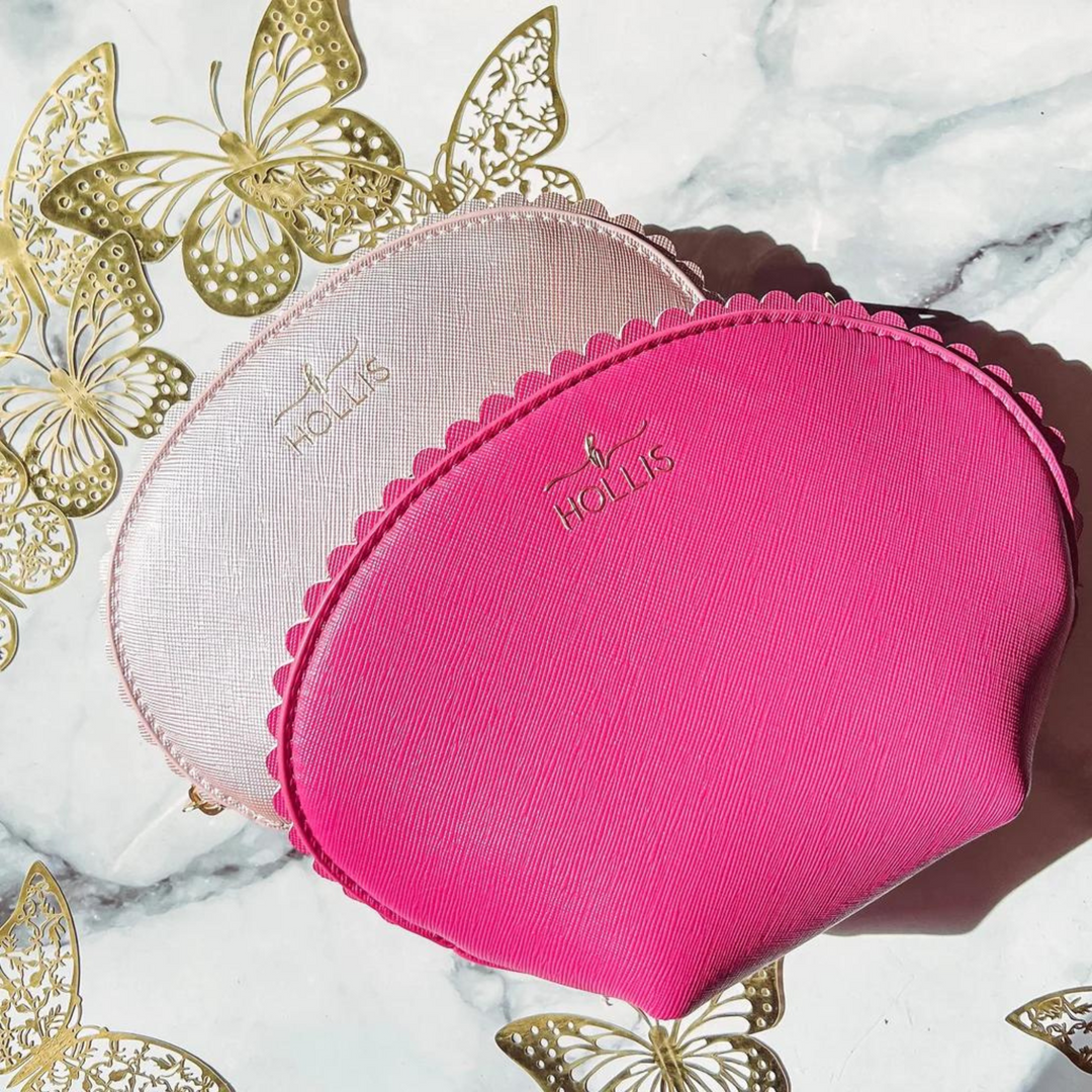 Pictured is a light pink dome shaped bag with a scalloped edge with the same bag in hot pink and a little bigger in front of the light pink one. These bags are pictured on a marble background with gold butterfly decoration.  