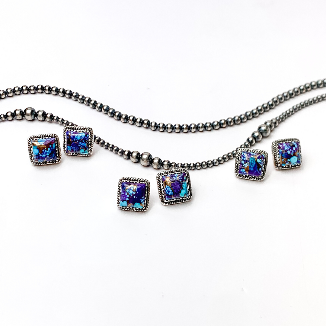 In the picture are handmade sterling silver square stud earrings with purple Mojave remix stones with a white background