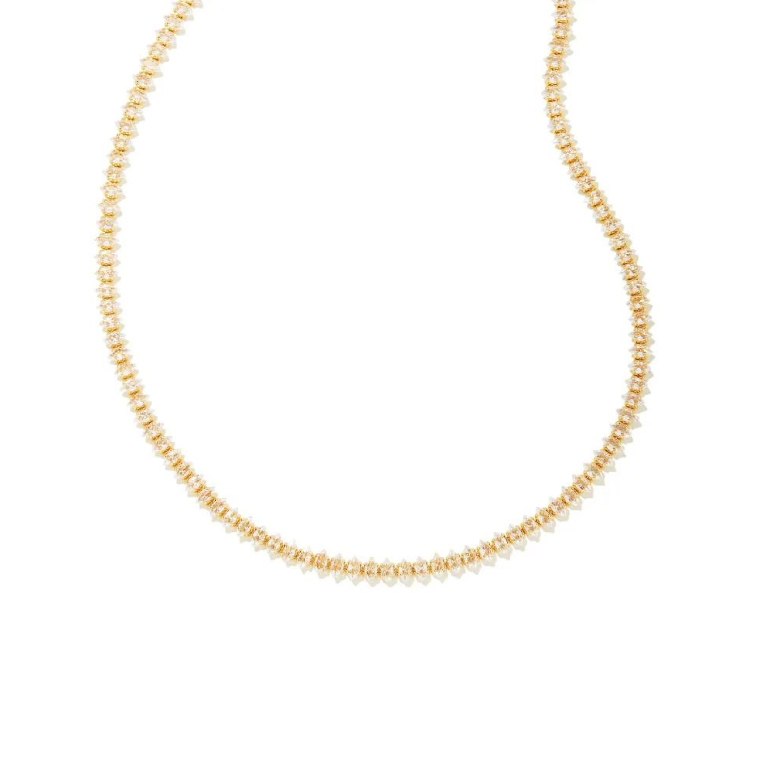 Pictured is a clear crystal tennis necklace in gold on a white background.