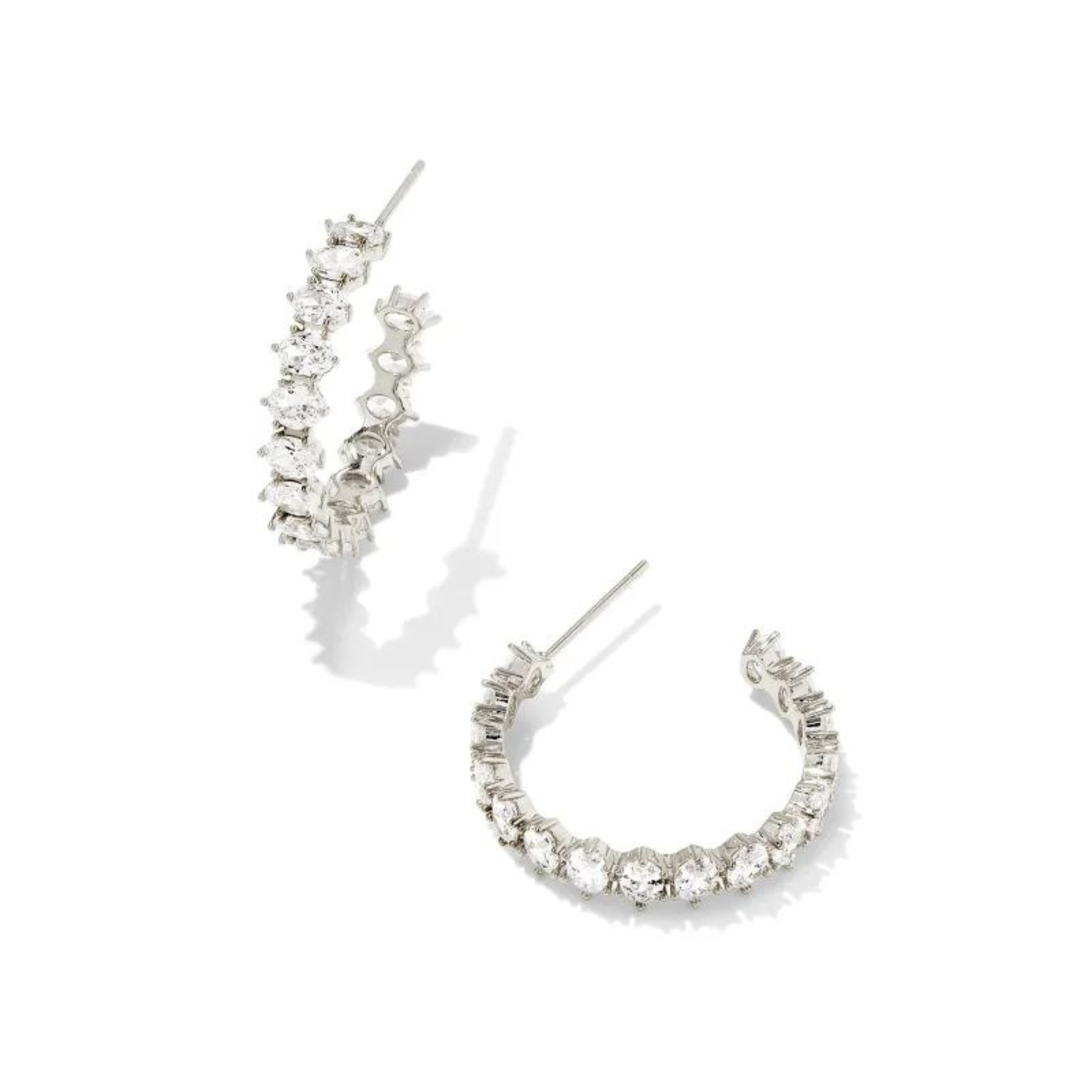 Pictured on a white background is a pair of silver hoop earrings with a oval, clear crystals. 