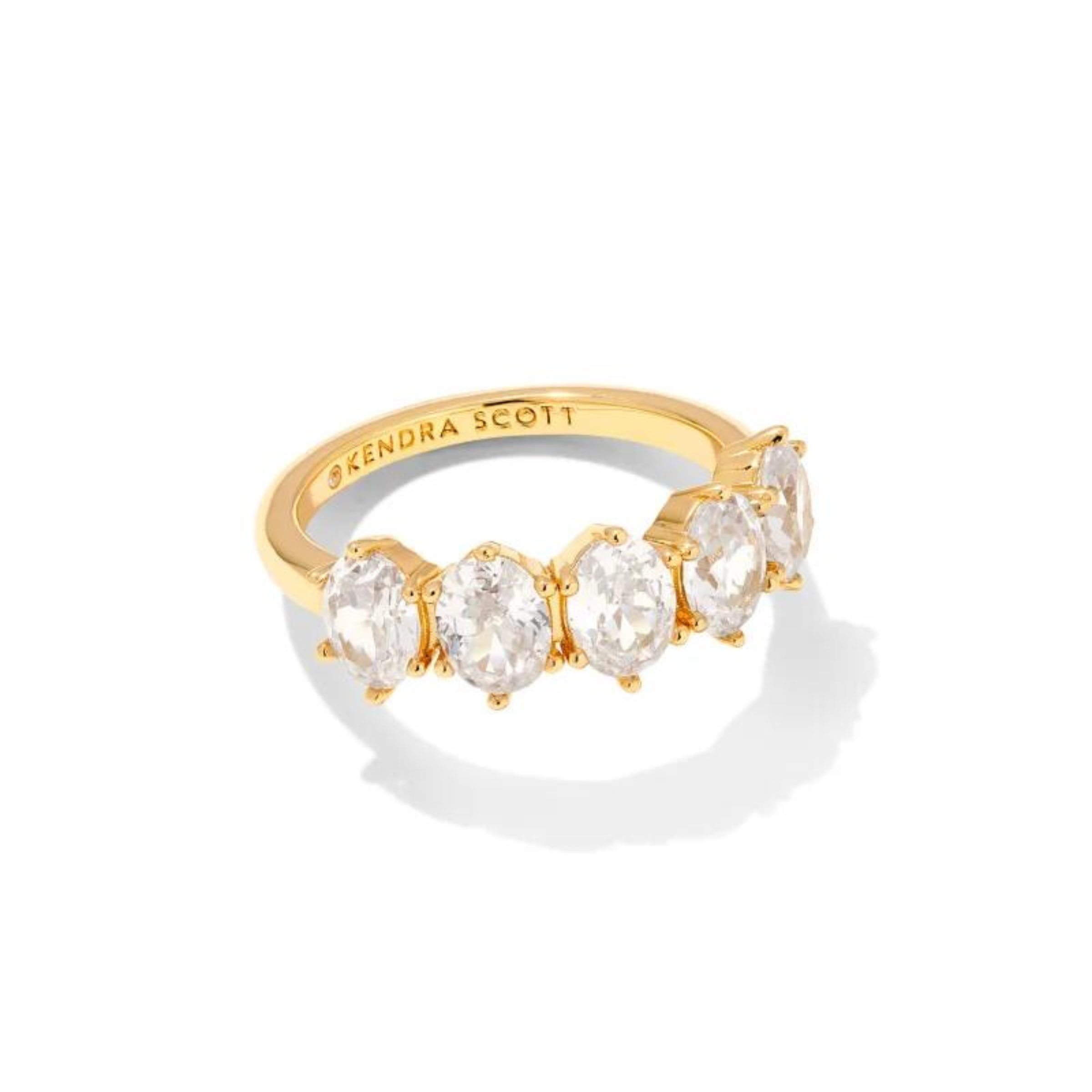 Pictured on a white background is a gold ring with five oval, clear crystals. 