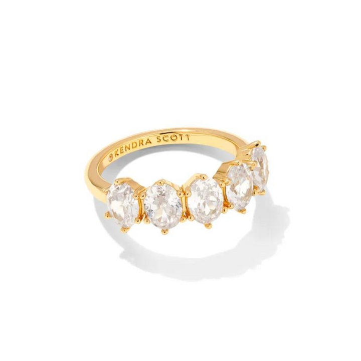 Pictured on a white background is a gold ring with five oval, clear crystals. 