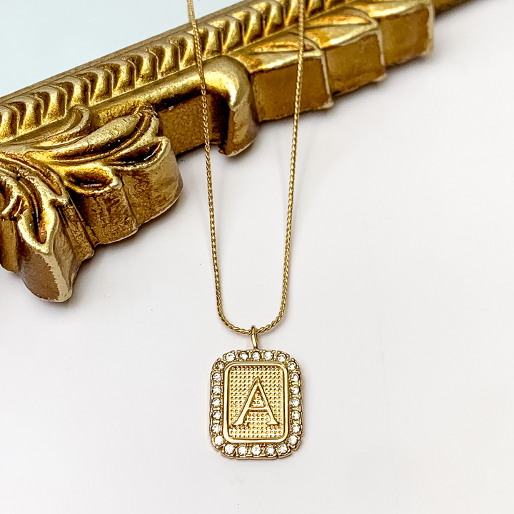 Gold Tone Chain Necklace with Rectangle Initial Pendant Outlined in Clear Crystals. Pictured on a white background with the top of the necklace on a gold frame.