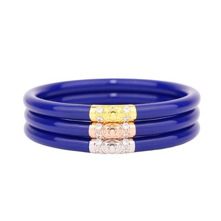 Pictured is a stack of three royal blue bangle bracelets on a white background. 